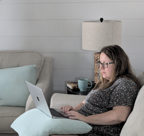 Woman working on computer while sitting on a couch. 